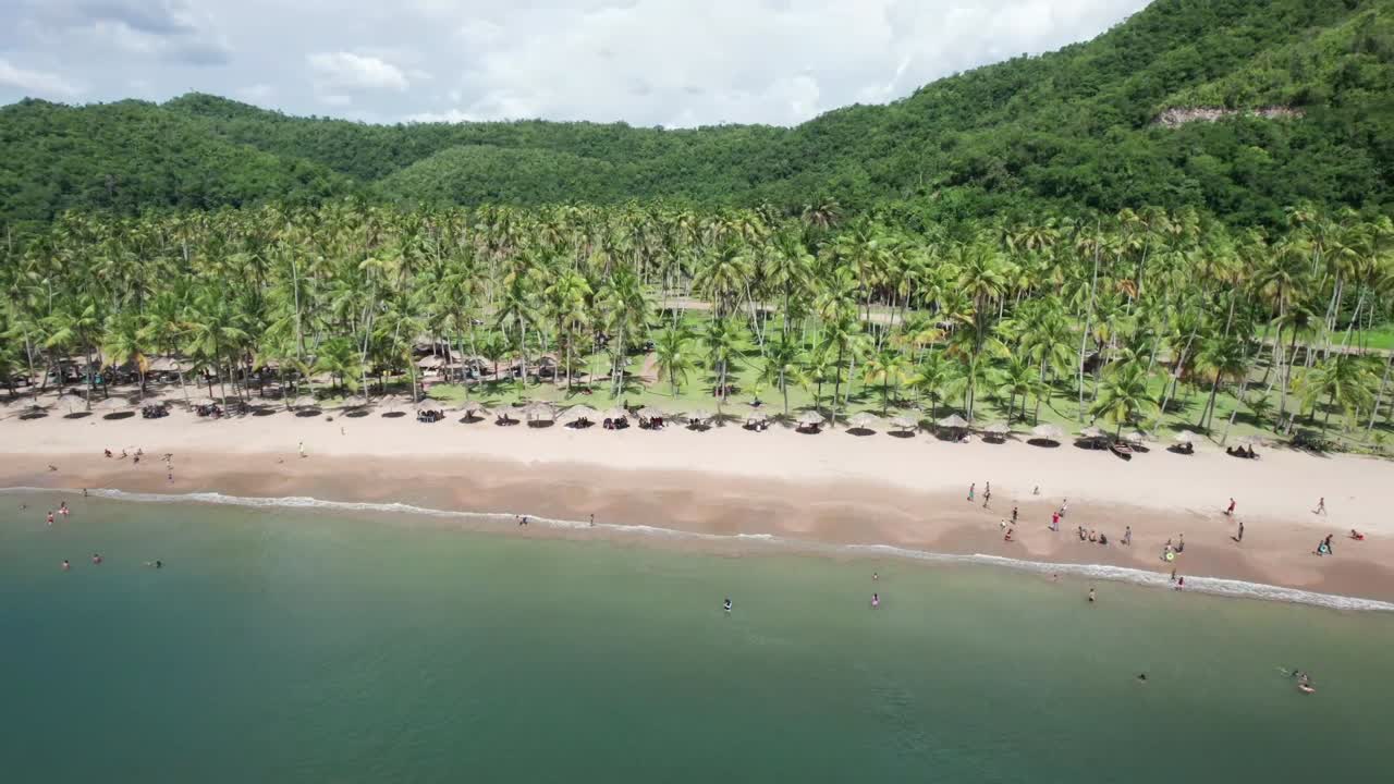 Drone shot of a beautiful remote tropical bay with palm trees, sandy beach, and a few people enjoying the water