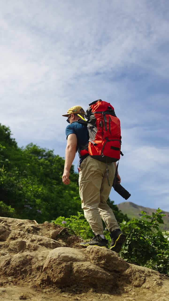 Uomo con zaino e macchina fotografica che fa escursioni in salita su un sentiero di montagna
