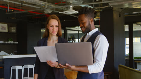 Vorderansicht-Eines-Jungen,-Coolen-Gemischtrassigen-Businessteams,-Das-In-Einem-Modernen-Büro-4k-Plant-Und-Einen-Laptop-Hält