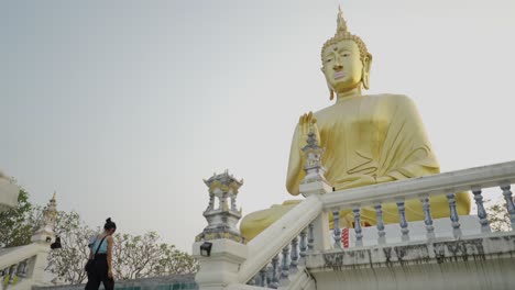 woman approaches a large golden buddha statue at a buddhist temple
