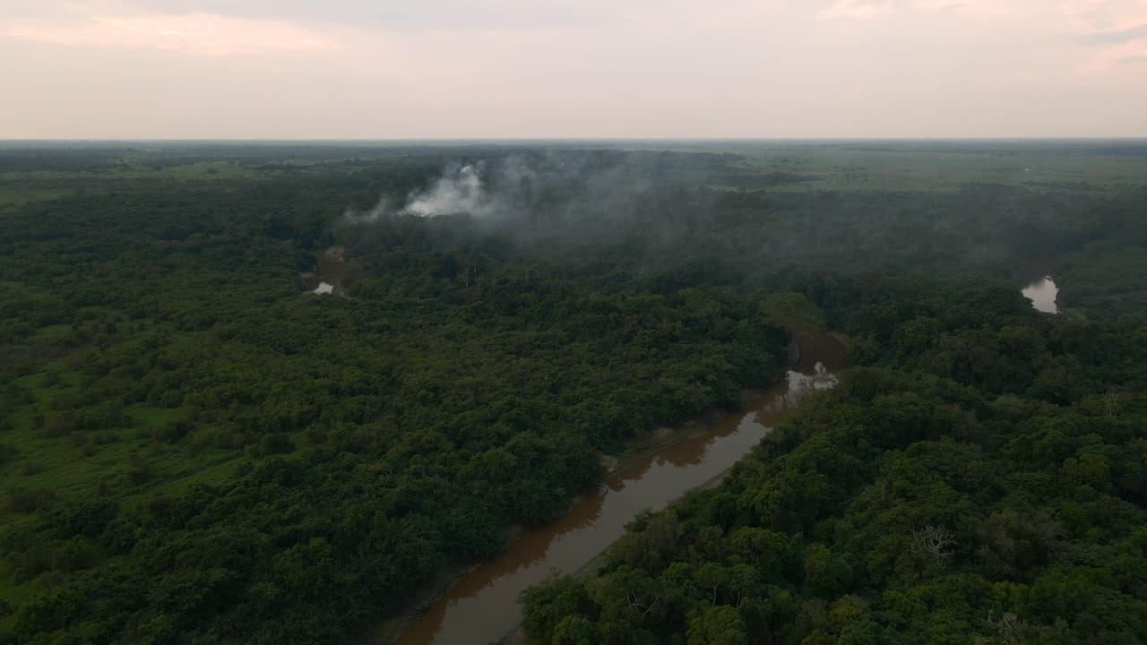 Aerial establishing overview of smoke rising above Bolivia, Rio Yacuma cutting through vast, unspoiled wetlands filled with wildlife