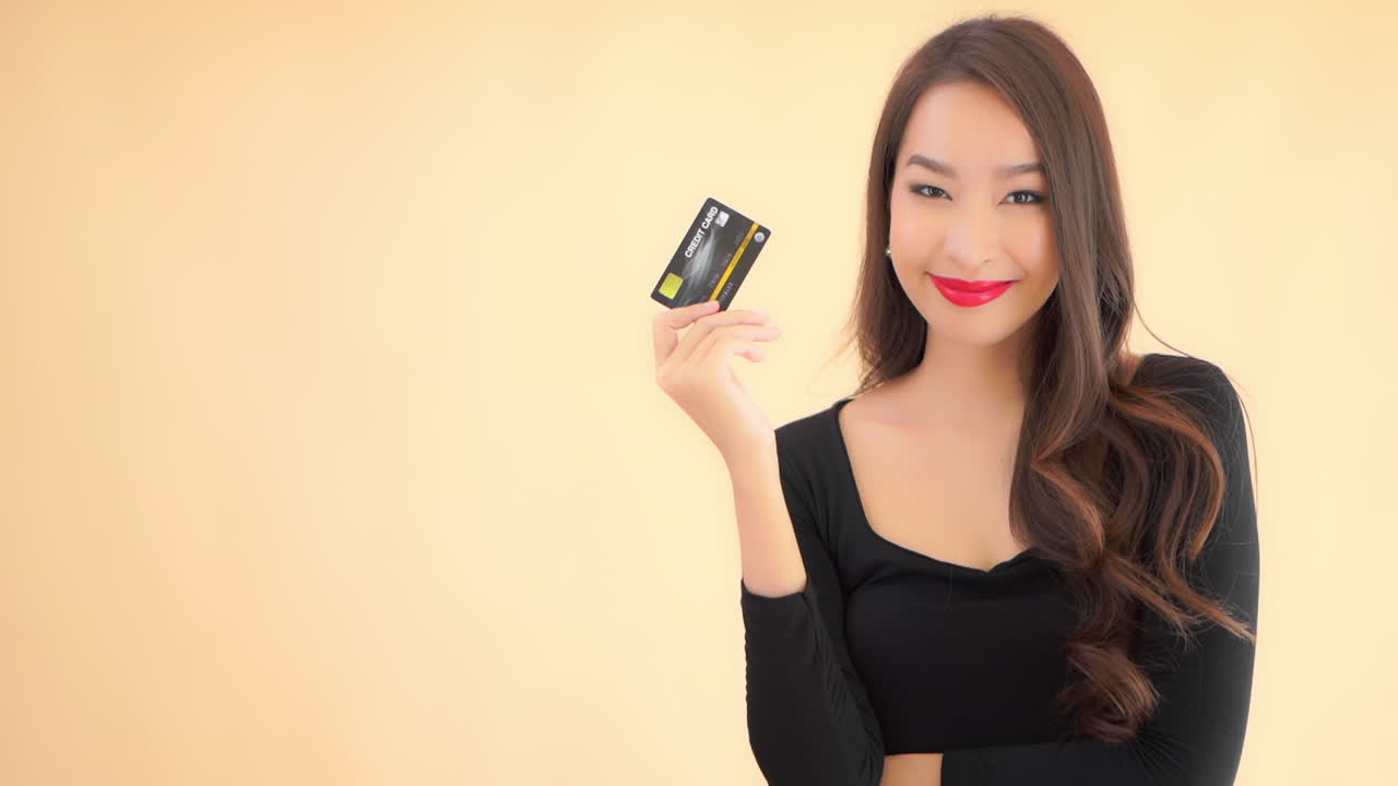 A close-up of a stunningly beautiful woman in a black dress suddenly smiles then produces a black and gold credit card. copy space