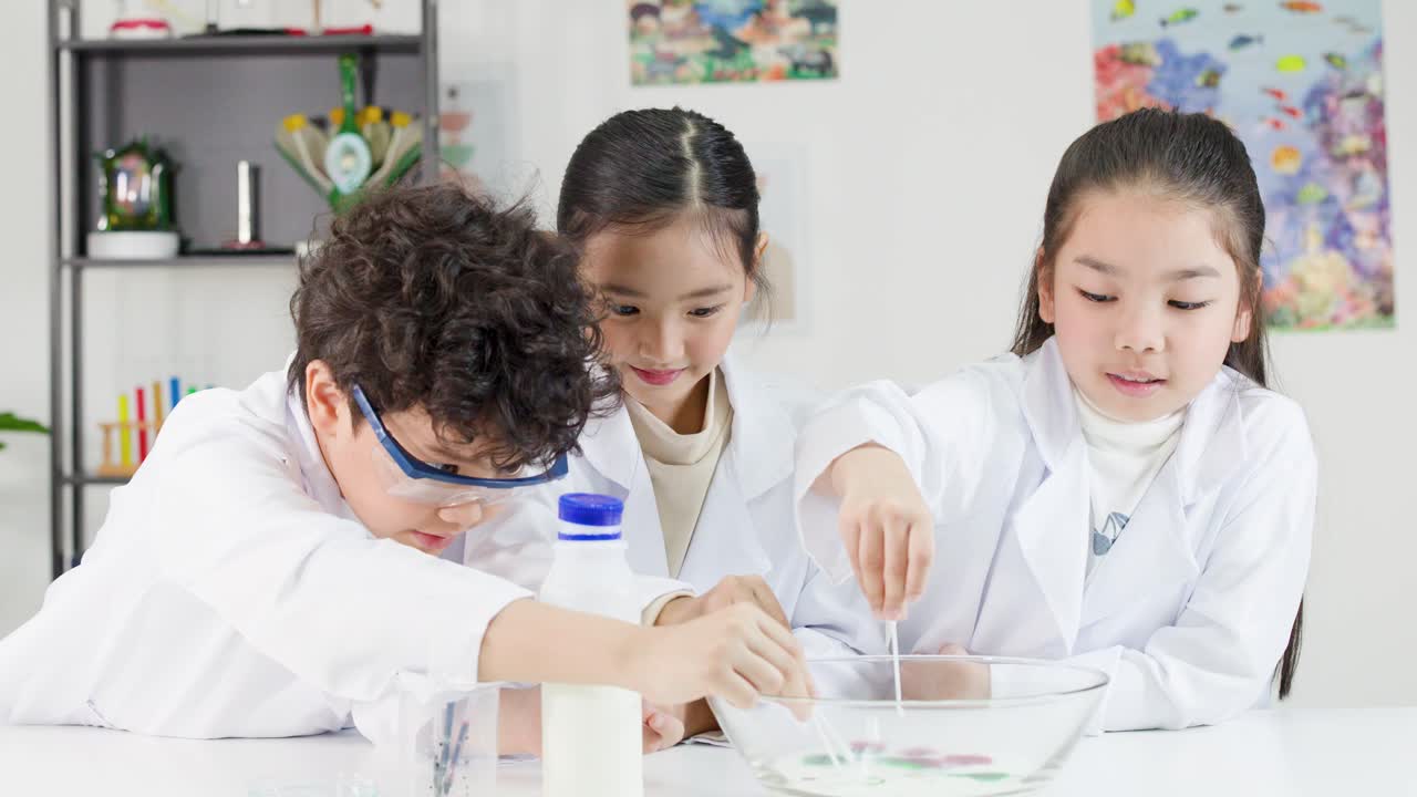 教室で白衣を着た3人の若いアジア人学生がカラフルな化学実験を行う