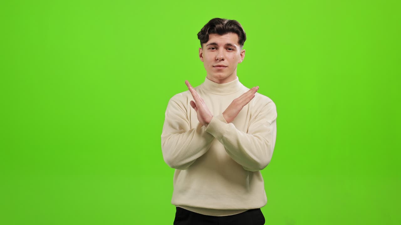 The man is standing and looking at the camera. He is crossing his arms and say Stop. He is standing on a green background. Green screen. 4K.