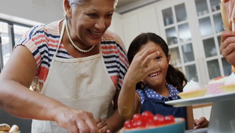 Girl-eating-a-cherry-while-making-cupcakes-with-mother-and-granny-4k