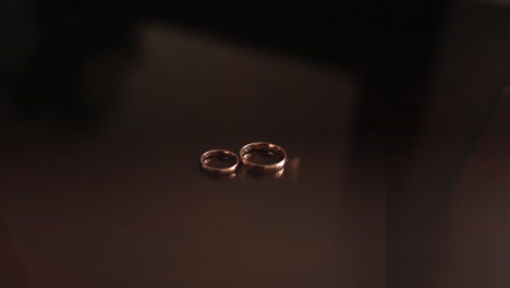 gold wedding rings resting on glossy wooden table under warm lighting