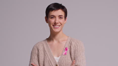 Studio-Portrait-Of-Smiling-Young-Woman-Wearing-Pink-Breast-Cancer-Awareness-Ribbon-Against-White-Background