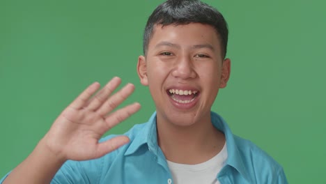 the happy young asian boy waving hand and say bye bye while standing on green screen in the studio