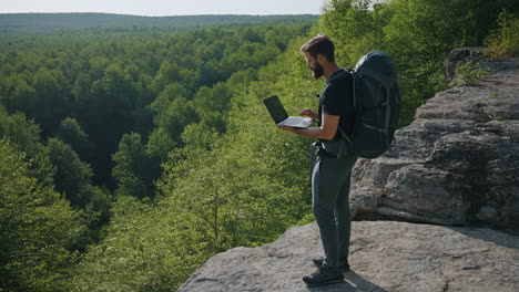 man with laptop on cliff overlooking forest