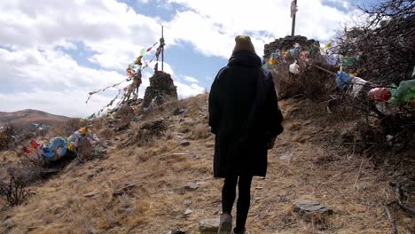 behind person walking up hill slow motion to sacred mountain prayer flags blowing in wind on mountain peak