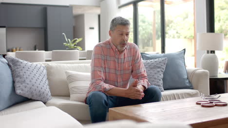 Worried-senior-biracial-man-sitting-on-couch-thinking-in-living-room,-copy-space,-slow-motion