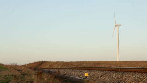 Red-cargo-train-moving-on-tracks-with-a-wind-turbine-in-the-background-at-sunset