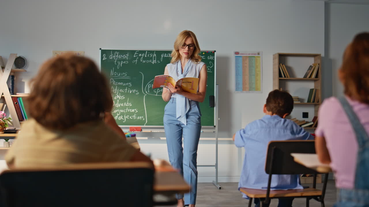 Educator teaching group pupils elementary school. Woman teacher reading book