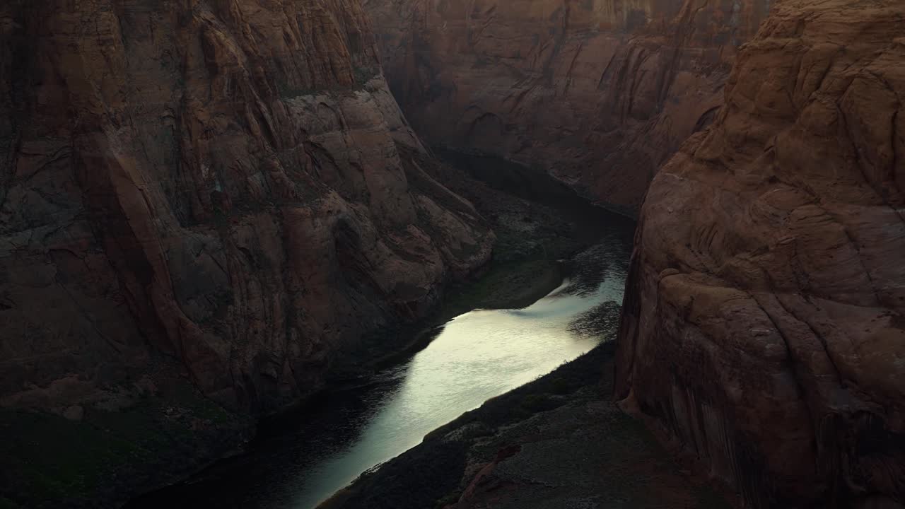 Handheld shot of the large calm Colorado river surrounded by huge orange sandstone rock cliffs caused by erosion near Page, Arizona during a desert evening in spring at dusk