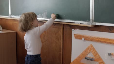 girl cleaning blackboard using a washcloth in classroom. education process