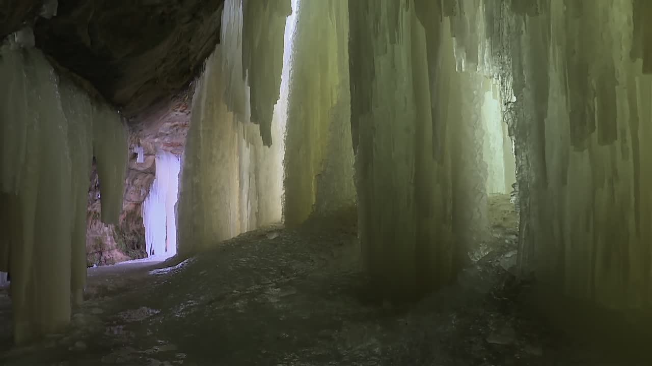 Tall vertical ice sheets rise from the ground inside Eben Ice Caves, tilt up view showing hanging icicles and cave roof