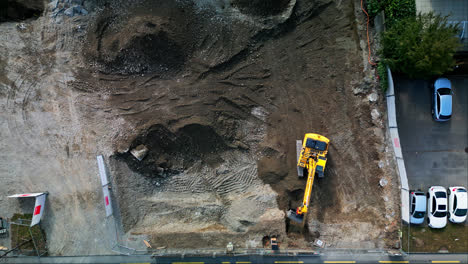 vista aérea estática de pájaro por encima de la excavadora amarilla que elimina la suciedad del sitio de construcción