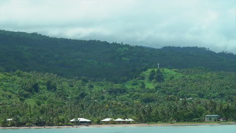 Boat-cruise-Fiji-port-marina-Garden-Island-Taveuni-Island-Pacific-Ocean-shoreline-beach-front-jungle-rainforest-Christian-Catholic-Cross-on-hillside-Viti-Levu-Group-landscape-nature-slow-zoom-in-pan