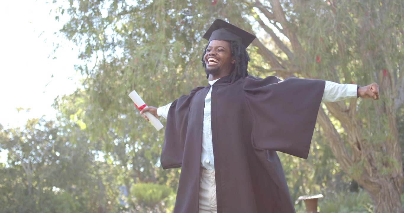 African American man running forward swinging arms holding diploma in gown celebrating in park