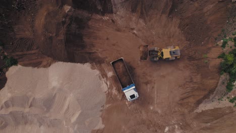 top down view of an excavator and truck are loading soil at the new neighborhood construction site