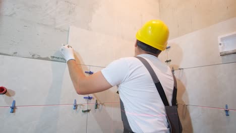 the hands of the tiler are laying the ceramic tile on the wall