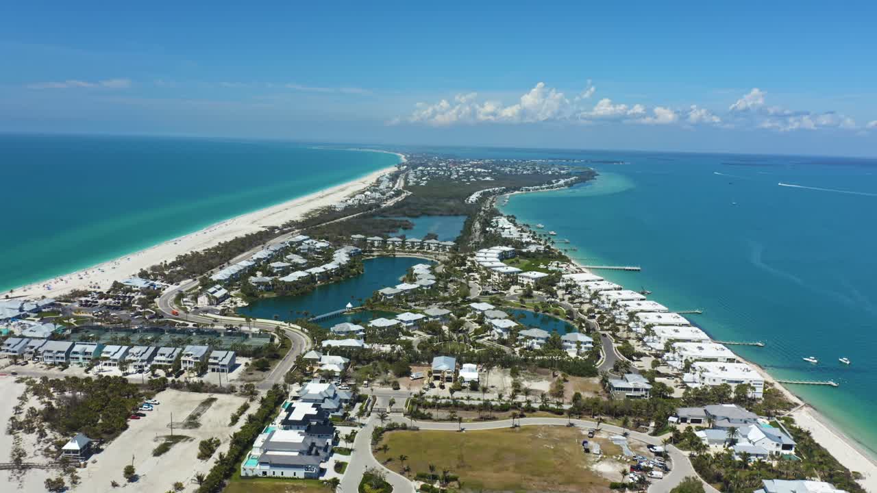 Aerial view of a luxury coastal neighborhood on a barrier island, bordered by the Gulf of Mexico and vibrant turquoise waters on a bright sunny day.