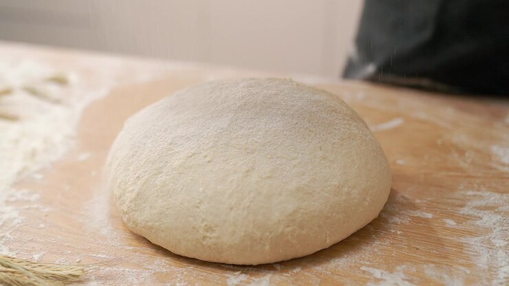 Flour Being Sprinkled Over Fresh Bread Dough on a Wooden Table