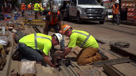 slow motion video of workers lining up new railroad tracks in a city. one worker smokes a cigarette while working, one helps and another supervises.