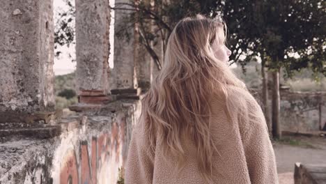 slow motion video of young millennial woman enjoy nature walking under a tree inside roman ruins and gently touching its leaves with sun flares coming through