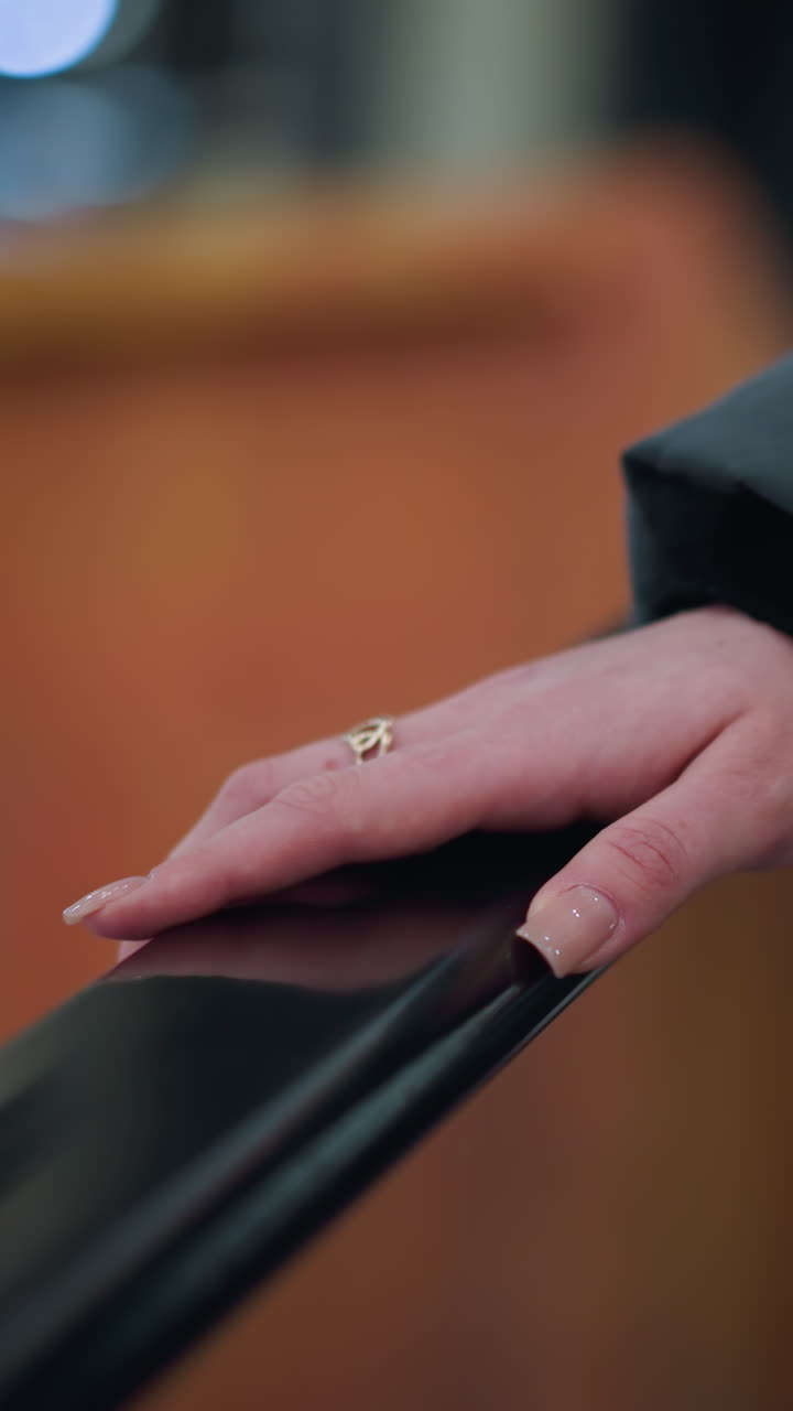 Close-up of well-polished nails placed gently on rail of moving escalator, framed with glass, the blurred background features a soft urban setting