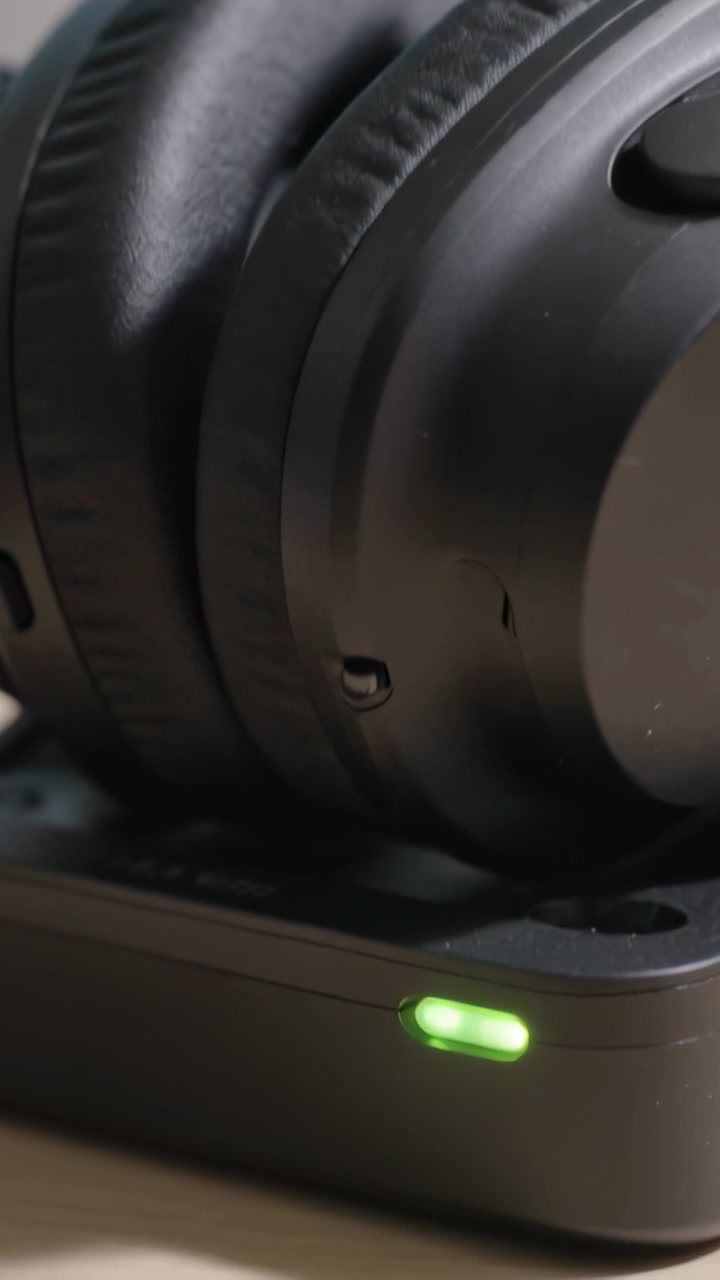Video verticale: Aggancio del padiglione di una cuffia over-ear nera su una base di ricarica sulla scrivania, ricarica indicata da un LED verde.