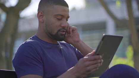 joven con una tableta en las manos en el parque, hablando por teléfono