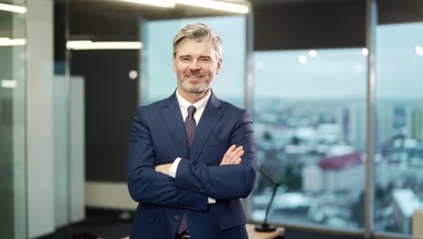 portrait of a mature adult gray bearded businessman in a formal suit and tie looking at the camera in a modern glass office