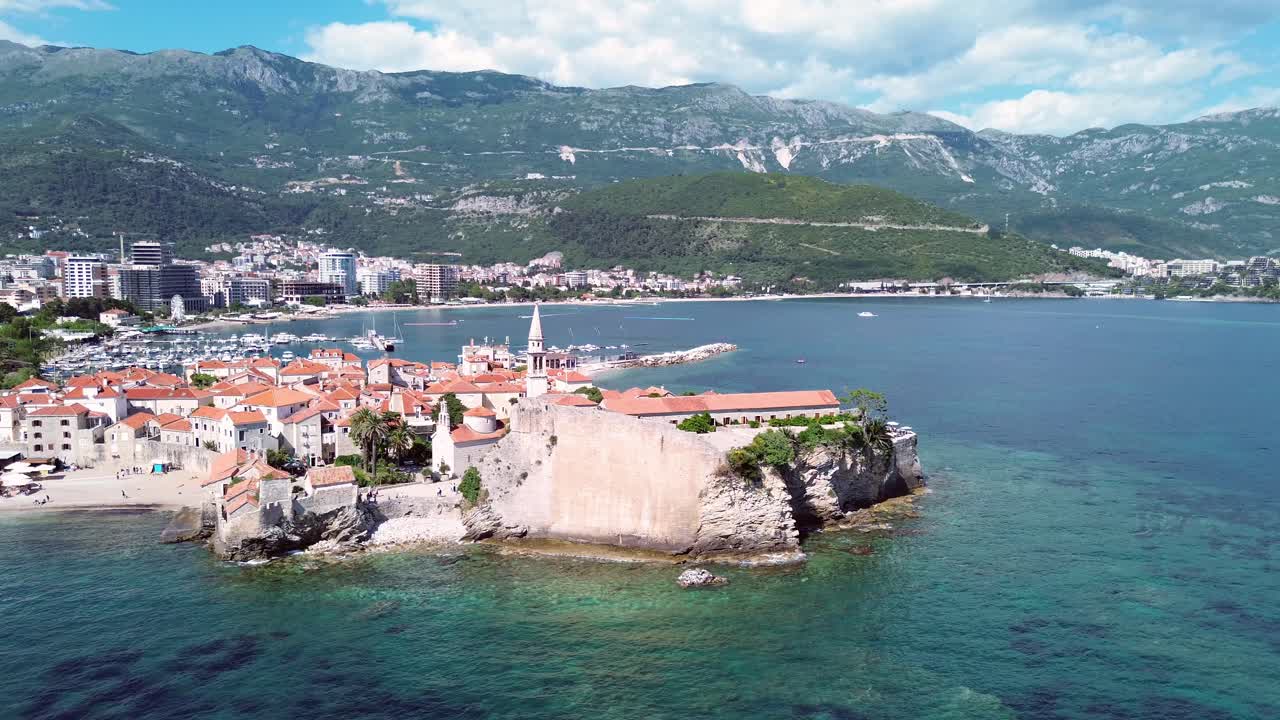 Old town medieval fortress, stone buildings contrasting new town highrise buildings and port in sunny daylight, Budva, Adriatic coast, Drone