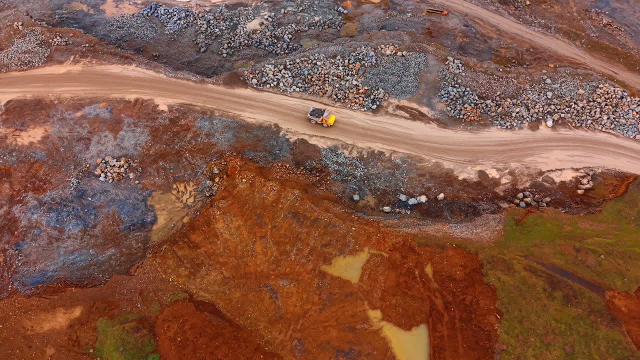 Truck on dirt road at site. A truck drives along a dirt road at a construction site surrounded by piles of rocks and earth in the background