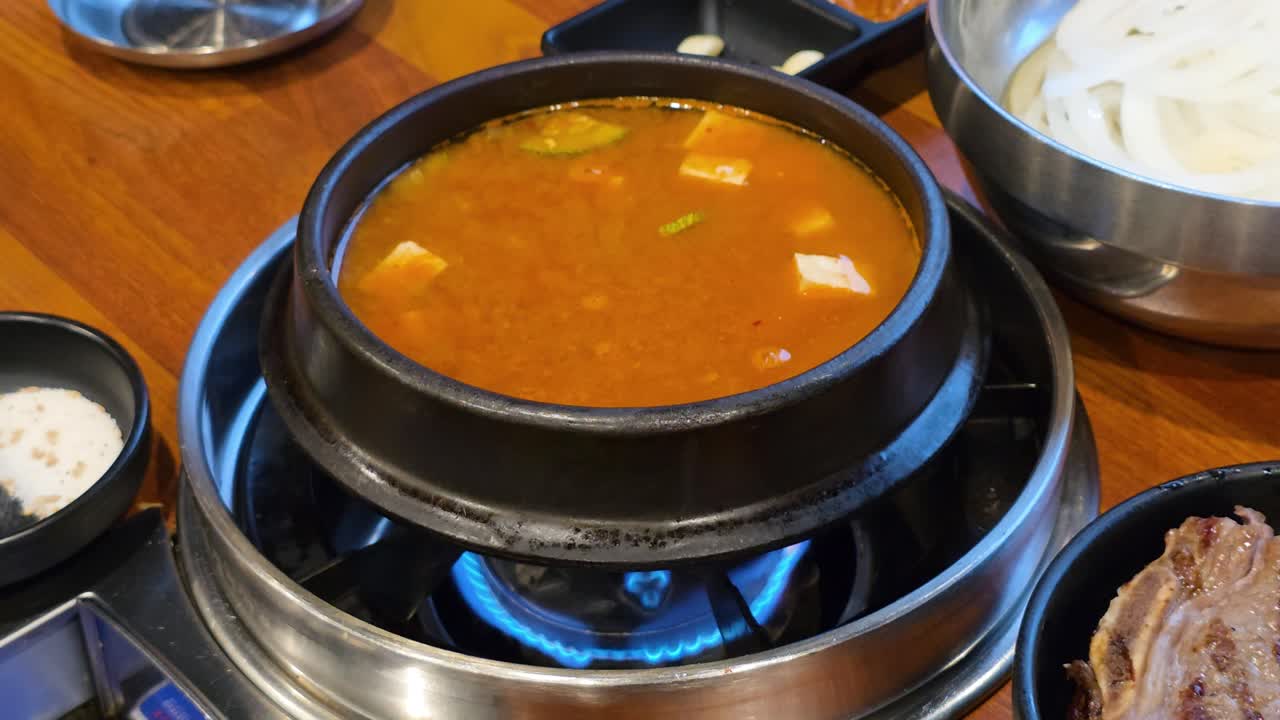 A close-up shot of a Korean traditional stew Doenjang jjigae - fermented soybean paste Korean cuisine stew with tofu seved in earthenware pot on a tabletop gas stove