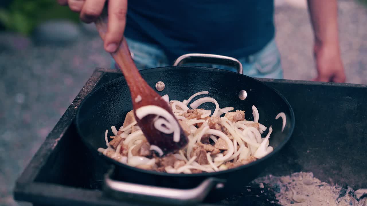 Close-up Travelling shot Young man makes pilaf in a cauldron on a grill on an open fire
