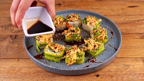 close-up of a plate of avocado sushi that is bathed in worcestershire sauce on a blue plate on a wooden table in a restaurant