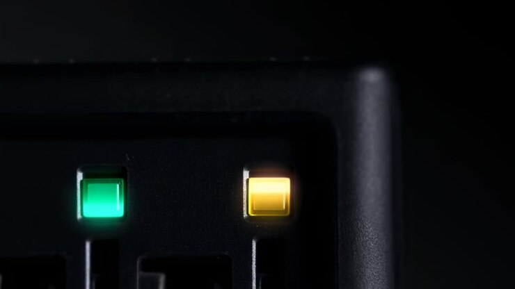 Close-up of a dark electronic control panel with two illuminated status indicators, one green and one amber, set against a minimal black background with a