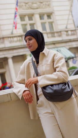 vertical video portrait of smiling muslim businesswoman wearing hijab and modern business suit standing outside city office buildings 8