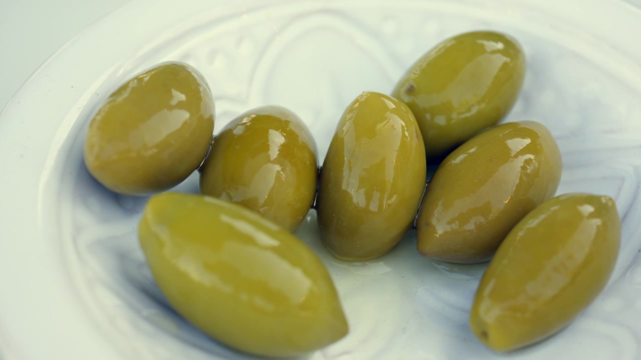 Olive verdi fresche su un piatto di ceramica bianco. Spuntino sano, antipasto o ingrediente per la cucina mediterranea.