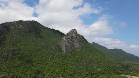 Reverse-aerial-footage-of-this-beautiful-mountain,-blue-sky-and-cotton-like-clouds,-some-farmlands