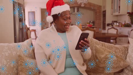 Animation-of-snowflakes-over-african-american-senior-woman-on-christmas-video-call-on-smartphone