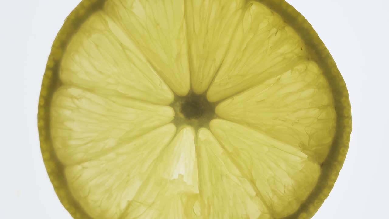 una rebanada de limón transparente giratoria sobre un fondo blanco.