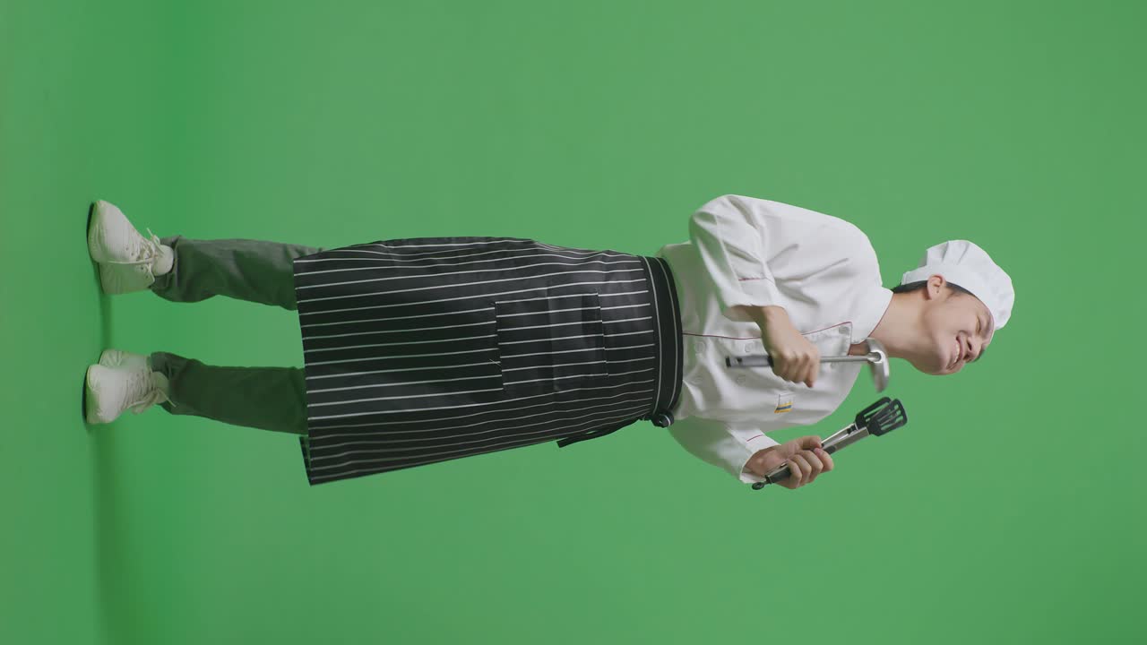 Full Body Of Asian Man Chef Holding Tongs And Ladle And Dancing While Standing In The Green Screen Background Studio