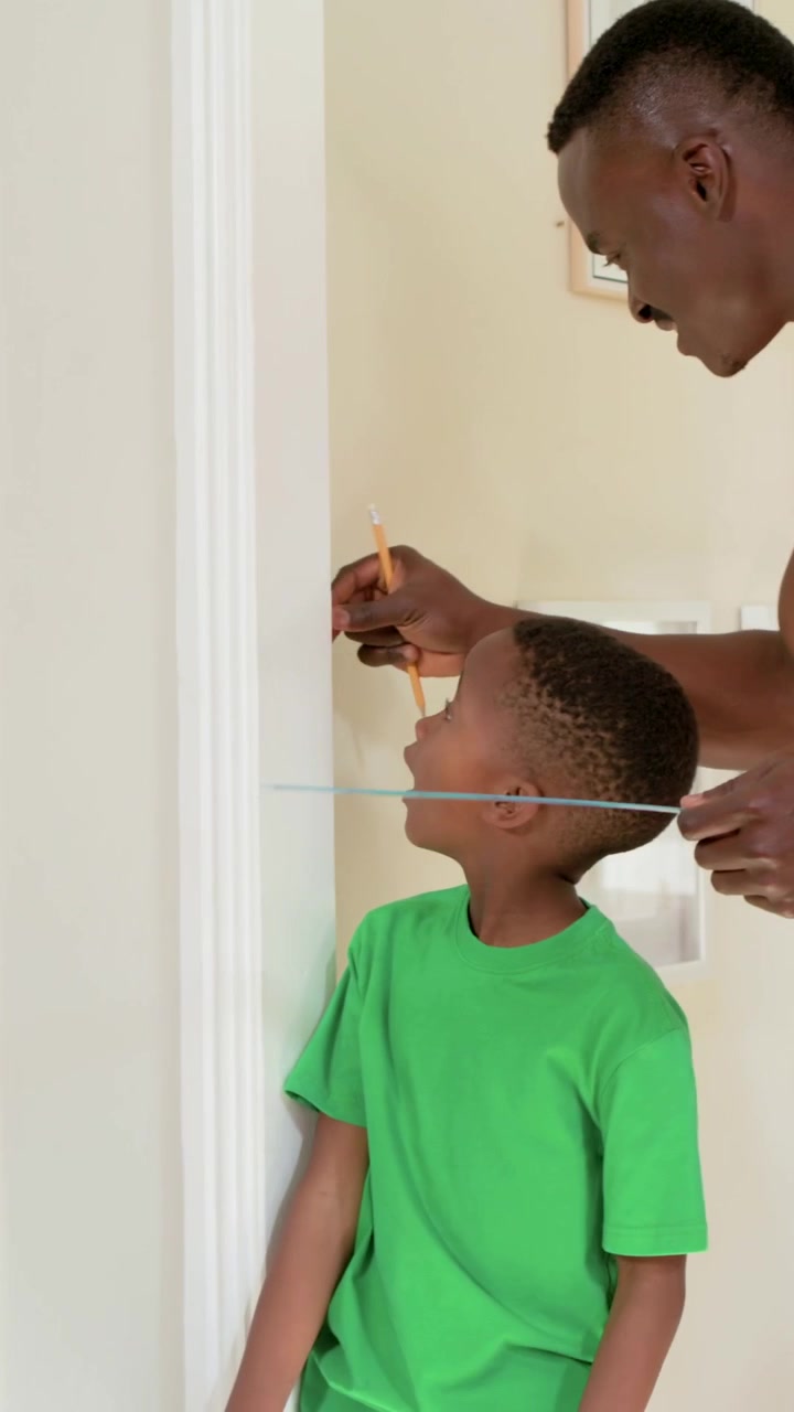 Vertical video: Placing pencil ruler dad measuring son by home trim marking height tee, copy space