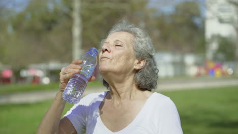 mujer mayor bebiendo agua de una botella de plástico al aire libre.