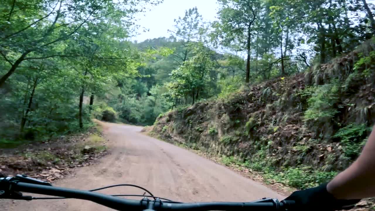 dos ciclistas andan en bicicleta por una carretera dentro de un bosque, una colina y un pueblo en guatemala, américa del norte