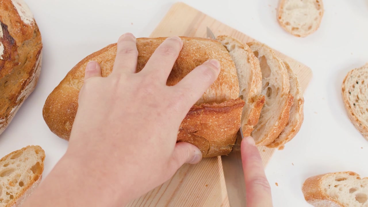 Vista dall'alto di mani che usano un coltello per affettare pane artigianale croccante su legno