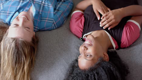 happy diverse female friends lying on bed and looking at each other at home, slow motion